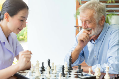 Senior retirement man playing chess with nurse at home